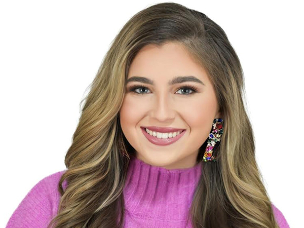 Smiling student with long brown hair wearing dangly earlings and a fusia turtleneck sweater
