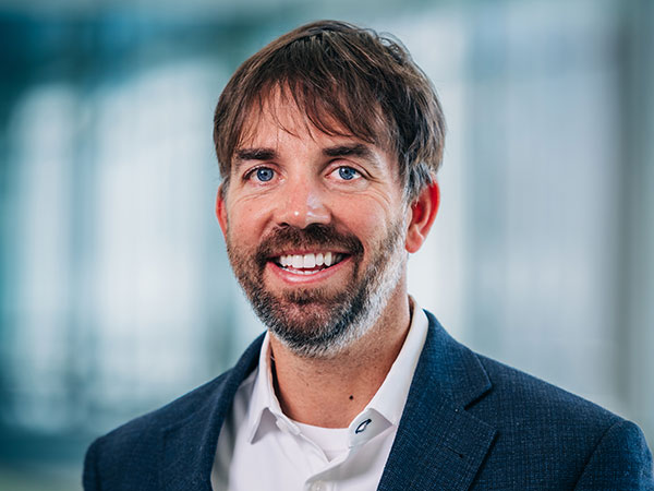Smiling man with short, dark hair and a beard dressed in a blue jacket