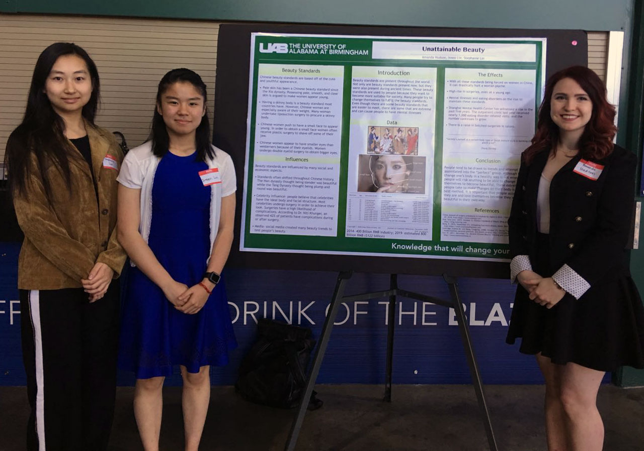 Three female students presenting a poster research project titled "Unobtainable Beauty."