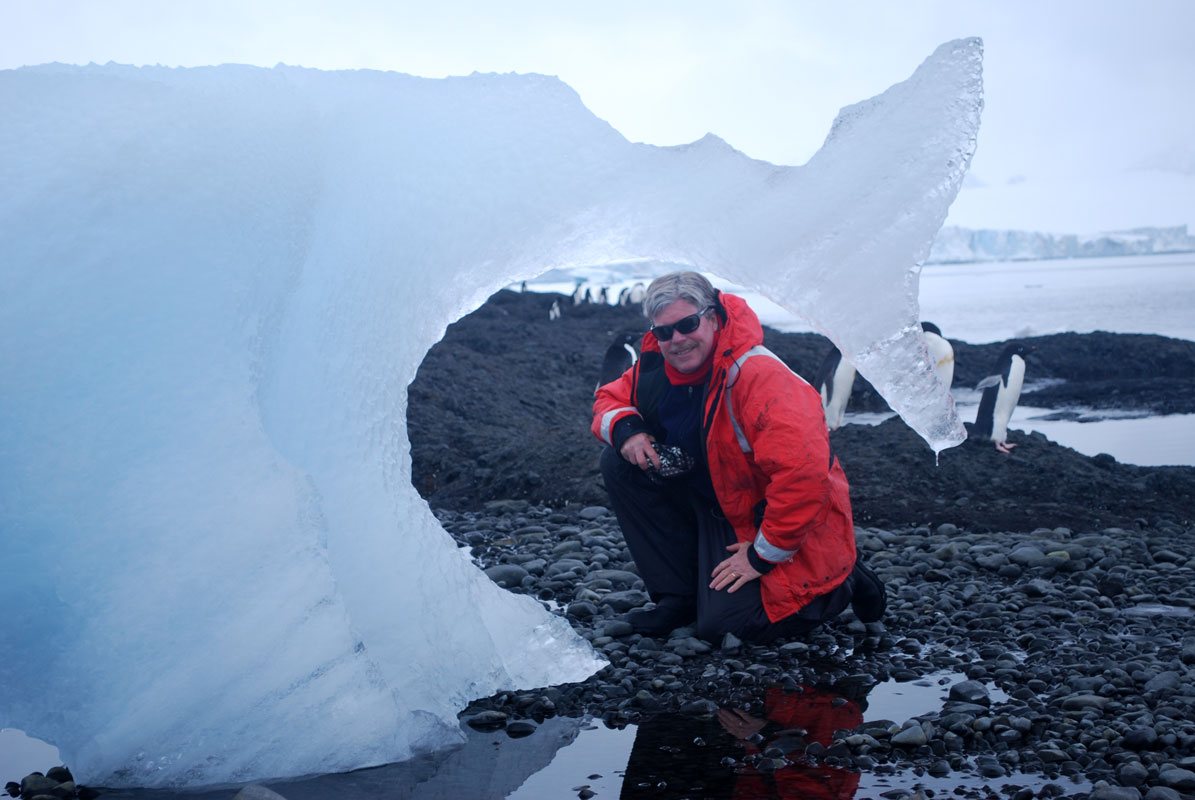 McClintock kneels under the arch of melting ice that resembles a whale tail. 