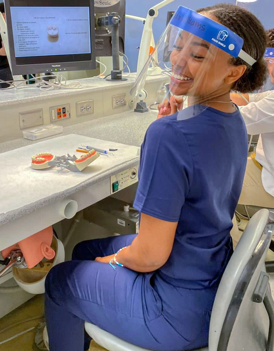 Jada Williams sitting at a desk in blue scrubs with a dental model in front of her. 