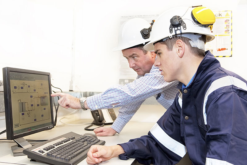 A senior and junior engineer discussing work in an on-site office. 
