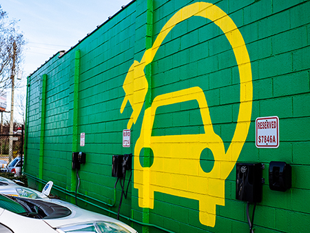 Large yellow electric vehicle painted on green background on concrete wall in front of the electric vehicle parking spaces, 2018.