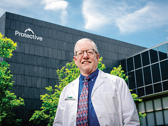 Environmental headshot of Dr. Steven Austad, PhD (Distinguised Professsor/Chair, Biology) wearing white medical coat while standing in front of Protective Life Corporation building on Highway 280, April 2021.