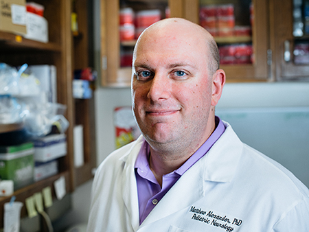 Environmental shot of Dr. Matthew Alexander, PhD (Assistant Professor, Pediatrics - Neurology) wearing white coat and standing in laboratory, 2018.