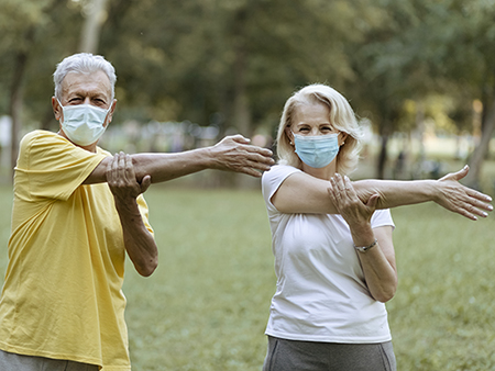 Joyful Senior Couple in Sportswear Stretching Outdoors in a Park on a Beautiful Spring Day While Wearing Face Protective Masks During Coronavirus Outbreak Living Active Healthy Lifestyle on COVID 19 Period