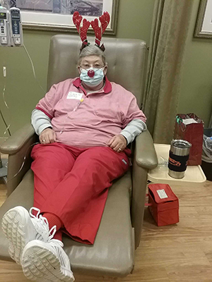 Charlotte Patterson dressed in all red with reindeer antlers and red nose sitting in chair for treatment. 
