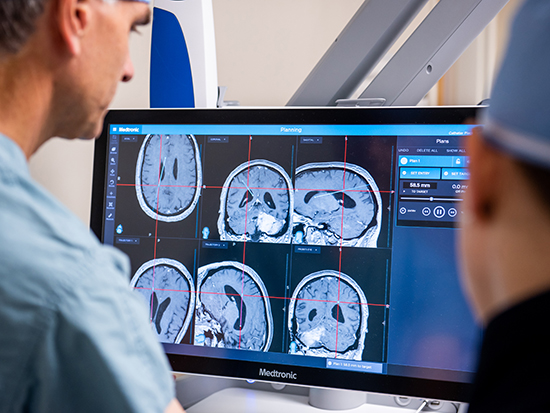 Back, Dr. James Markert, MD (Professor and Chair, Neurosurgery) is looking at brain imaging on a computer during Operation Preparation before a surgery, 2020.