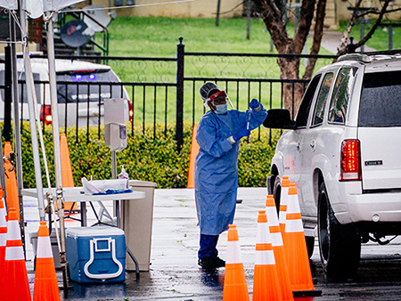 From side, a medical professional is wearing a medical gown, mask, and gloves while standing beside a parked SUV underneath a tent at the Downtown COVID-19 Testing Site sponsored by UAB Medicine and the Jefferson County Department of Health on March, 23, 2020.