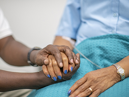 Elderly woman is comforted by a medical professional during the Covid-19.  Focus is on their hands.  The medical staff is holding the woman's hand.
