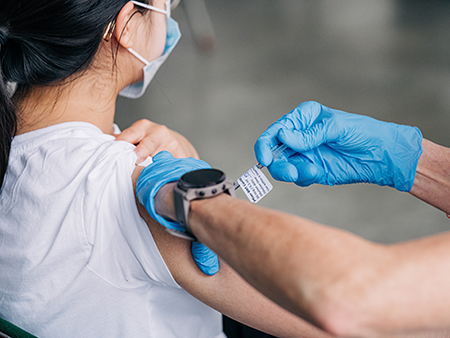 Female student is wearing a face mask while getting vaccinated against COVID-19 by a health care worker at Bartow Arena, May 18, 2021.