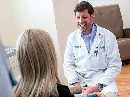Dr. Charles Leath, MD (Professor, Gynecologic Oncology) is sitting beside and talking to a Gynecologic Oncology patient in the Women and Infants Center, 2020.