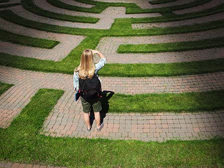 A woman teenager student stands looking through the puzzling maze of schooling and the education system, forecasting the way forward and searching for the path to her goal. Concept of student facing uncertainty to their education, life and future career.
