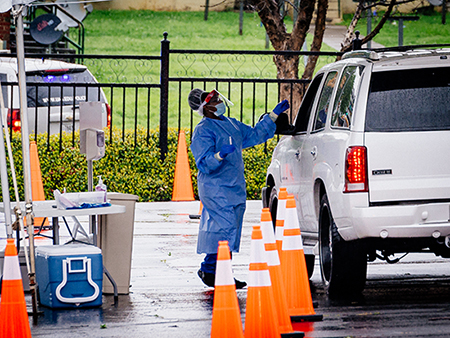 From side, a medical professional is wearing a medical gown, mask, and gloves while standing beside a parked SUV underneath a tent at the Downtown COVID-19 Testing Site sponsored by UAB Medicine and the Jefferson County Department of Health on March, 23, 2020.