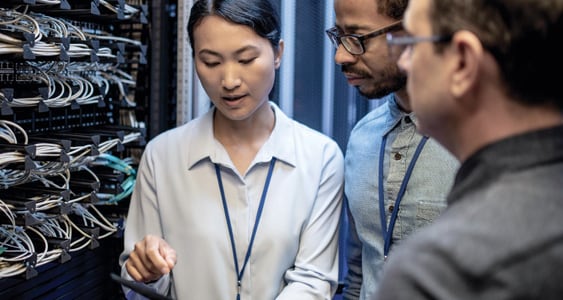 Three multiracial IT workers - one woman and two men discussing a nearby server.