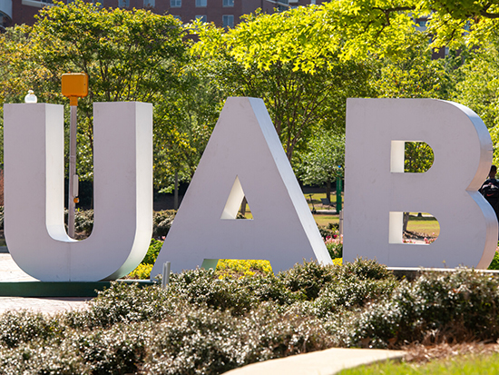 Large letters that spell U A B sit on the sidewalk outside the Hill University Center on UAB's campus