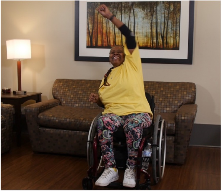Black woman in wheelchair in her living room lifting weights. 