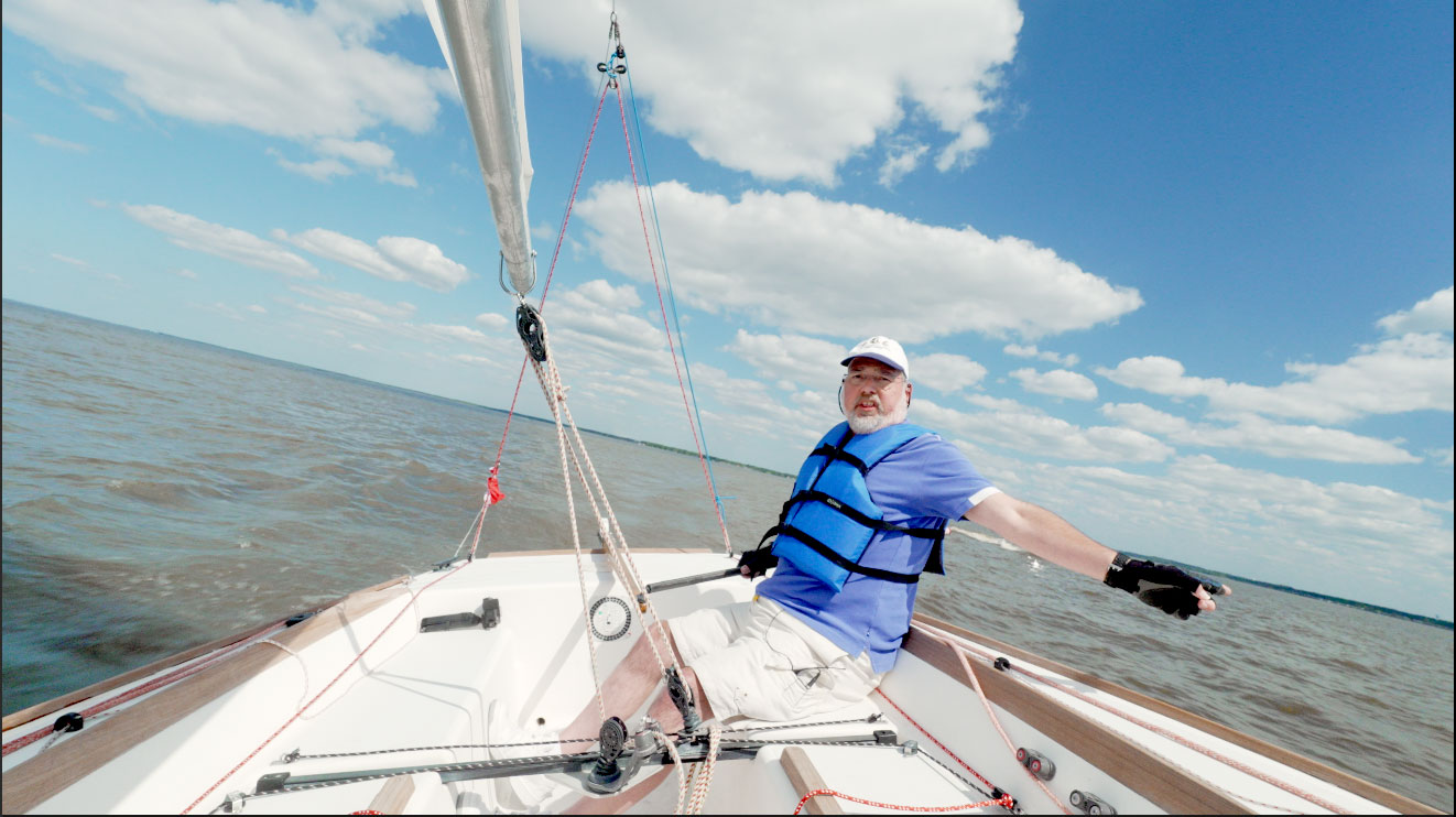 Dt. Craford sails his boat on open water, blue sky with scattered clouds stretching before him. 