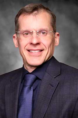 Keith McGregor wearing a dark suit with subtle plaid pattern and purple tie. 