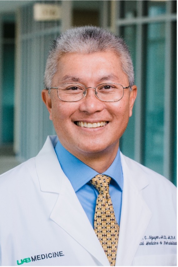 Dr. Vu Nguyen has short salt-and-pepper hair and wears glasses, and is wearing a blue button-up shirt, yellow patterned tie, and a white doctor's coat. 