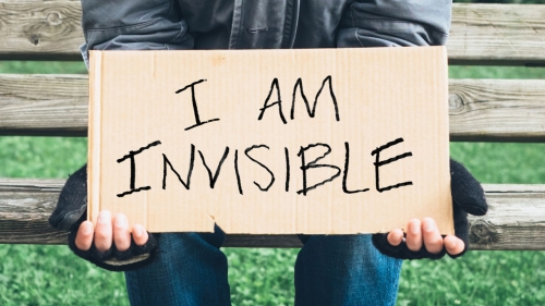 Photo of man holding cardboard sign with headline: I Am Invisible